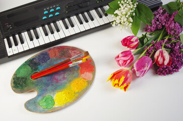 Synthesizer keyboard, art palette, brushes, a bouquet of tulips on a light background.