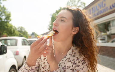 Woman eating tasty pizza outdoor in street cafe. Fast food takeaway in sunny day.