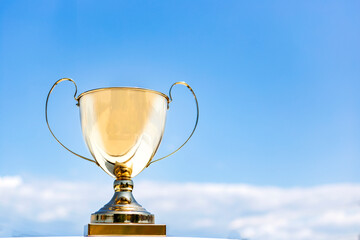 Golden trophy cup on blue sky background. Copy space for text. victory and success concept