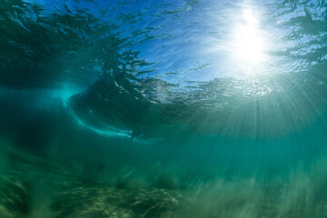 Fototapeta na wymiar underwater wave crashing with sun rays and a surfer