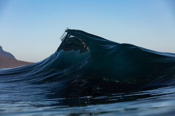 dark blue wave breaking on a shallow reef with blue sky background