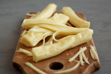 Organic String Cheese on a rustic wooden board on a gray background, side view. Close-up.