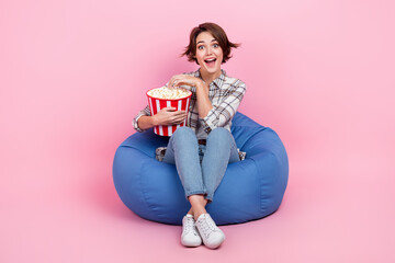 Full body photo of cheerful positive lady sit cozy bag eat popcorn watch movie isolated on pink color background - obrazy, fototapety, plakaty