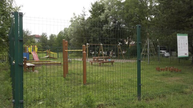 A children's playground behind a tall fence surrounded by trees
