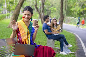 concept of lgbtq lifestyle,lgbtq happy pride month,woman transgender in colorful rainbow dresses sitting in the park,using laptop internet online waved hello someone while studying outdoors on weekend
