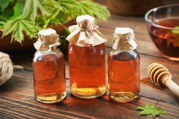 Three bottles of maple syrup or healthy tincture and spring maple leaf. Bowl of maple syrup and wooden dipper on background.