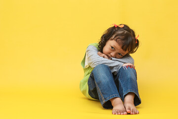 Sad Asian little girl sitting and hugging knees over yellow background with copy space. Children...