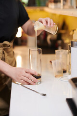 Barista adding condensed milk in tall glass with espresso