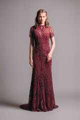 Bead embellished floral short sleeve halter maxi dress in maroon. Dark red unique transparent evening gown with a train. Beautiful young brunette woman's studio portrait. Female elegant clothes.