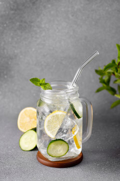 mason jar of cold detox water with cucumber and lemon or lemonade on grey background