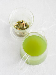 matcha green tea in a glass jar beside tea leaves and infused herbs