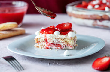 Italian traditional dessert tiramisu with strawberries. One piece of cake on a plate closeup,...