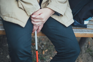 コートを着た視覚障害者の男性が白杖を持って休んでいる