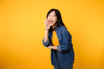 Young asian woman wearing yellow t-shirt denim shirt with open mouths raising hands screaming announcement isolated on yellow background. Lifestyle portrait concept.