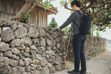 白杖を持った視覚障害者の男性が沖縄で石垣の近くを歩いている