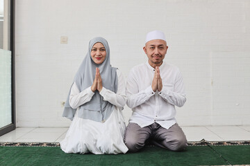 Asian muslim couple showing congratulate hands gesture Eid Mubarak and sitting together at home, asking forgiveness on eid moment. 