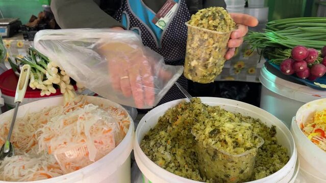 a woman pins salted cabbage into a bag, the hands of a seller in the market, the counter of the Russian market. Pickled vegetables, cabbage, in large bowls on the counter, outdoor market, salted veget