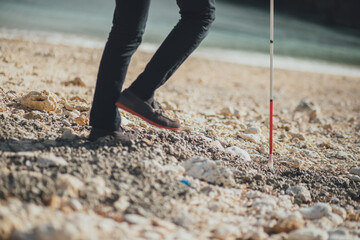 白杖を持った視覚障害者の男性が沖縄の浜辺を歩いている