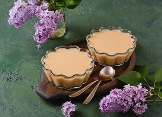 Blancmange, almond milk jelly in transparent bowls on a brown tray against a green concrete...
