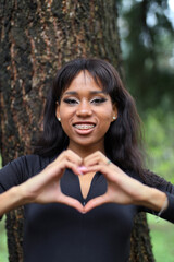 Dark-skinned woman shows a heart in the park.