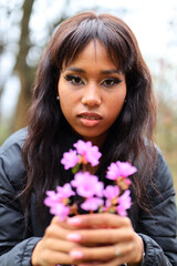 Naklejka premium A african brunette woman found purple flowers in the park.