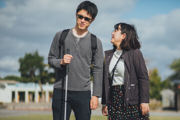 白杖を持った視覚障害者の男性が女性と沖縄を旅している