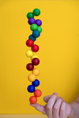 Balancing colored plastic balls on a finger on a yellow background.