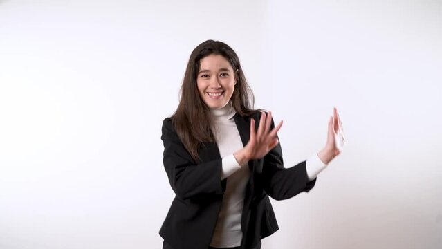 Smartly dressed playful young woman with dark hair against white background dancing while moving her hips sideways and making with her hands circling gestures 
