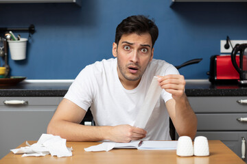 Close up of unhappy man sitting at the table, stressed and confused by calculate expense from invoice or bills, have no money to pay mortgage or loan. High prices and spending money concept