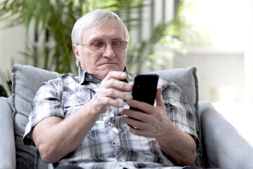 Portrait of aged man sitting on the armchair and talking on phone with his relatives	