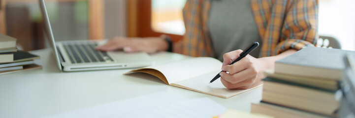 Young woman student busy study make notes in notebook and using laptop concentrated online training...