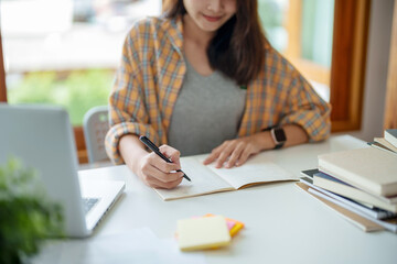 Young woman student busy study make notes in notebook and using laptop concentrated online training...
