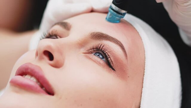 Professional dermatologist in medical gloves doing hydro peeling procedure for beautiful woman patient in cosmetology clinic. Close up facial treatment.
