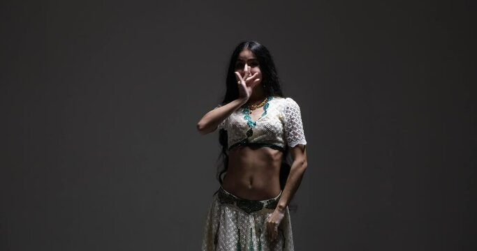 Young Indian dancer in a white saree with intricate details and sparkling jewelry will enchant you with her beautiful dance moves and expressions. She perform on a dark background.
