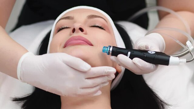 Professional dermatologist in medical gloves doing hydro peeling procedure for beautiful woman patient in cosmetology clinic. Close up facial treatment.
