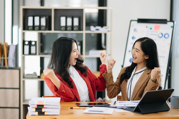 Two Asian businesswoman discuss investment project working and planning strategy with tablet laptop computer in office.