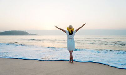 Happy woman standing on the beach with hands up.