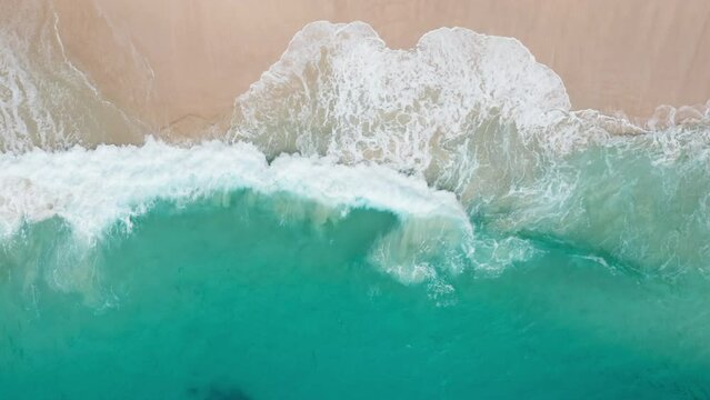 Aerial view of beautiful footage while turquoise raging sea waves breaking on sandy coastline. Drone top shot of beach with strong power ocean water and foam waves. Paradise. Big swell. Natural world.