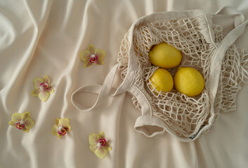 Flat lay tropical orchids and lemons in crochet net bag. Summer aesthetic idea. Minimal creative concept.