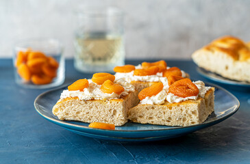 Focaccia sandwiches with prosciutto, soft cheese stracciatella, dry apricots on a blue plate, ingredients, fresh drink backside over dark blue and grey background