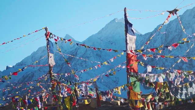 Slow motion shot of prayer flags waving in the wind in front of the snow covered Himalayan mountains at Kunzum Pass on the way to Kaza from Manali in Himachal Pradesh, India. Prayer flags at Kunzum. 