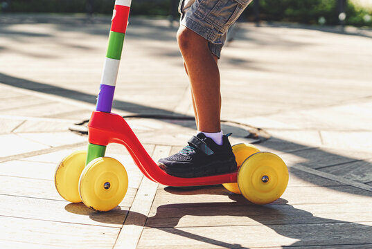 Kid Riding Toy Scooter, Feet Detail - Closeup of a child's legs and feet on a toy scooter. Wearing shorts and sneakers, the child's identity remains anonymous.