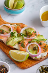 Open sandwiches with salted salmon, cream cheese, onions, capers, cucumber and microgreens on wooden board with white kitchen table background. Seafood. Healthy food. Close up. Copy space
