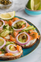Open sandwiches with salted salmon, cream cheese, onions, capers, cucumber and microgreens on white kitchen table. Seafood. Healthy food. Close up. Copy space
