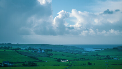 Cloudy sky over the green rolling fields of southern Ireland. Landscape of the southern coast of Ireland with blue sky and clouds. Green grass field under white clouds.