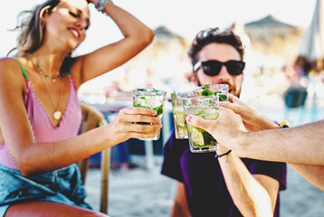 Young Friends Toasting with Mojito Cocktails at Beach Bar: Group of friends at the beach bar toast with mojito cocktails, hands focus, blurred background.