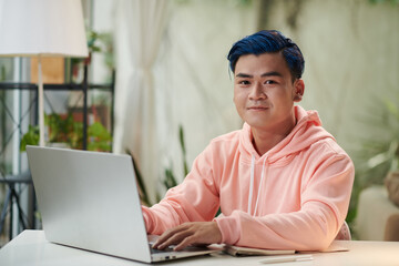 Portrait of smiling smart young man programming on laptop at home