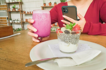 Woman is taking pictures of healthy food and drinks with her smartphone in a restaurant. Girl filming cafe dish and beverage. Concept for gen z, millenials, content creator, food photography, vlogger.