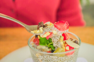 Woman scooping fruit chia pudding with various toppings such as mint leaves, strawberries, raisins, sliced ​​almonds and chia seeds. Concept for healthy eating, fat loss, organic food, vegan diet.
