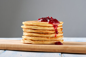 Pancakes with red berry jam on the wooden table.